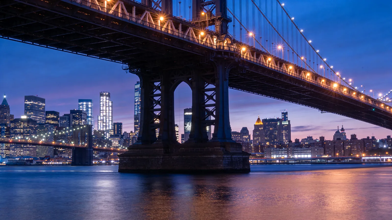 Brooklyn Bridge fully illuminated at deep twilight with the East River reflecting lights — things to do in NYC on July 4th Brooklyn vantage point
