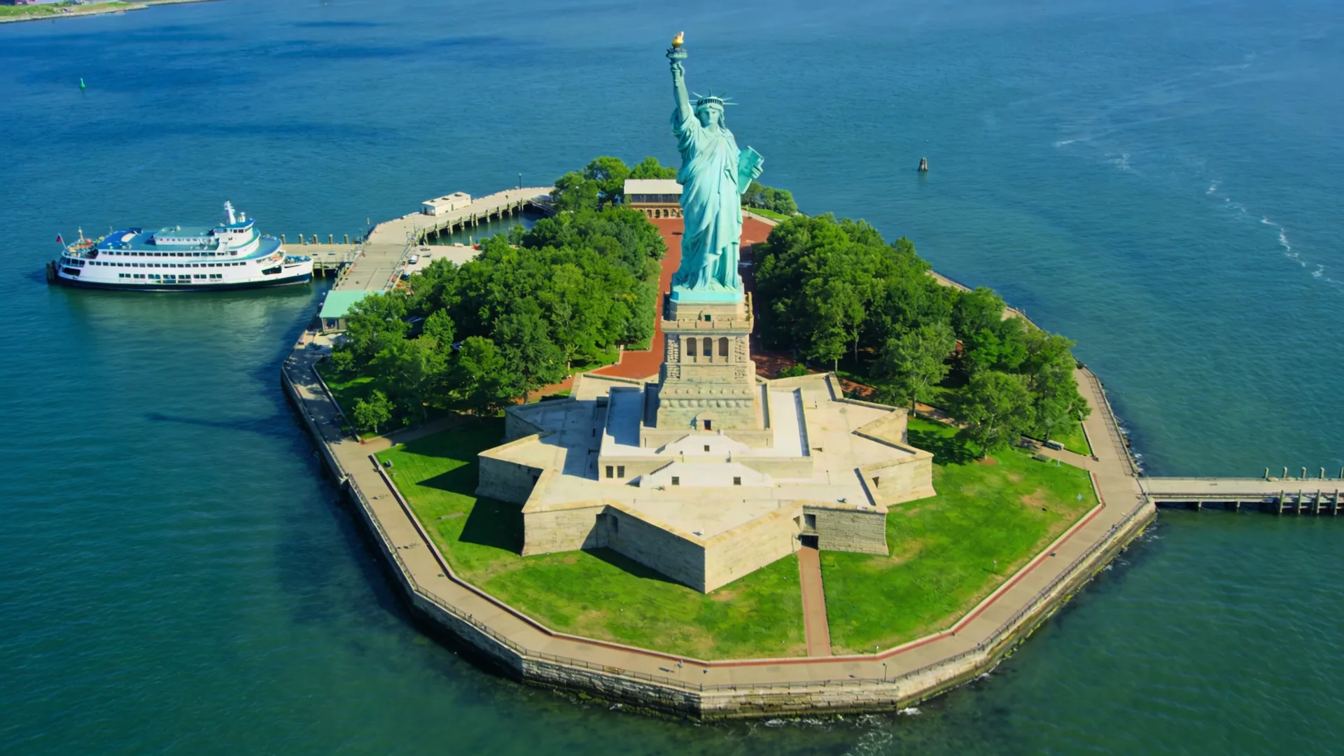 Wide aerial view of Liberty Island in summer with ferry docked — Statue of Liberty cruise in summer overview