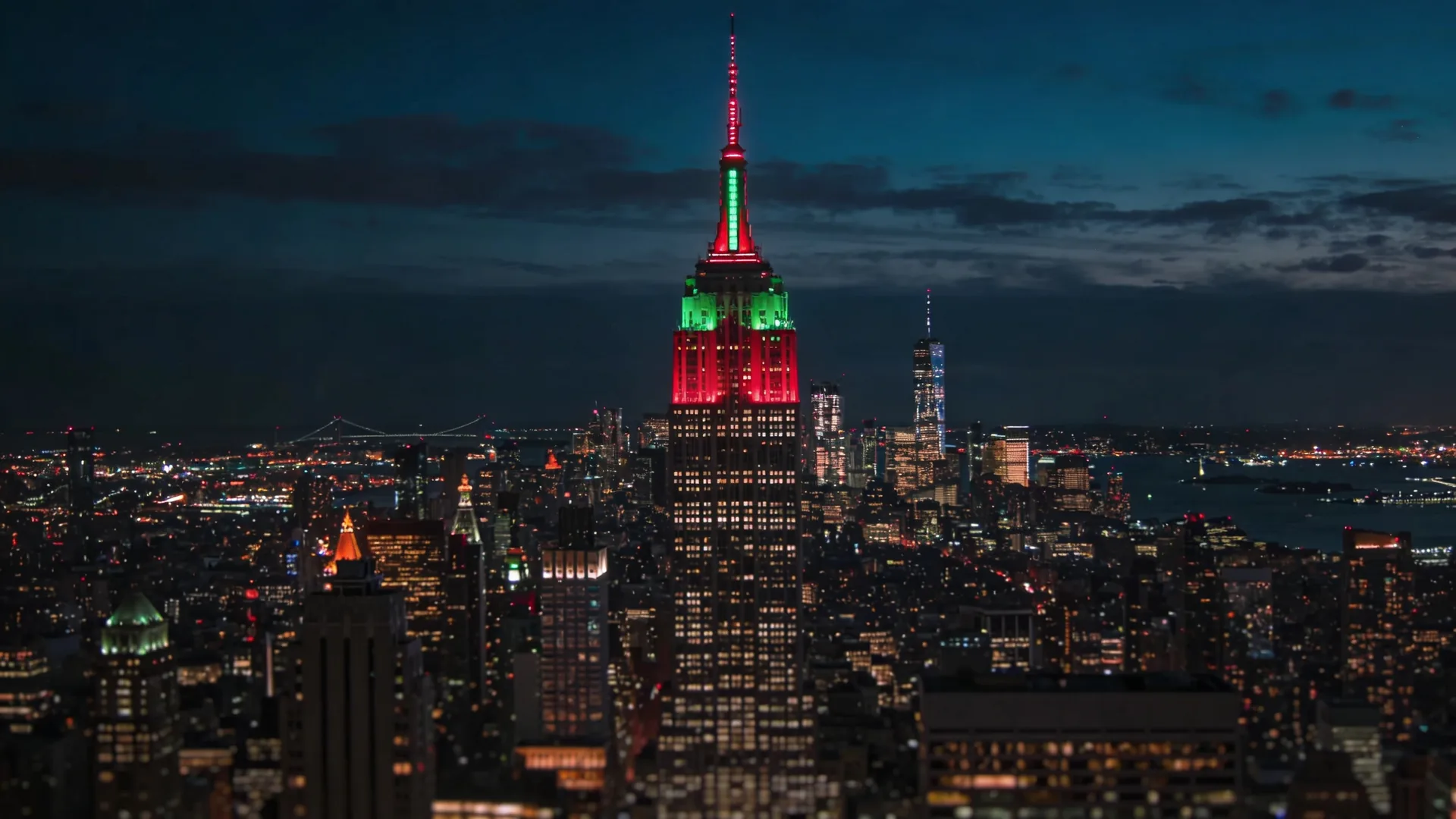 Empire State Building spire lit in red and green Christmas colors viewed from across midtown — Empire State holiday lights iconic shot