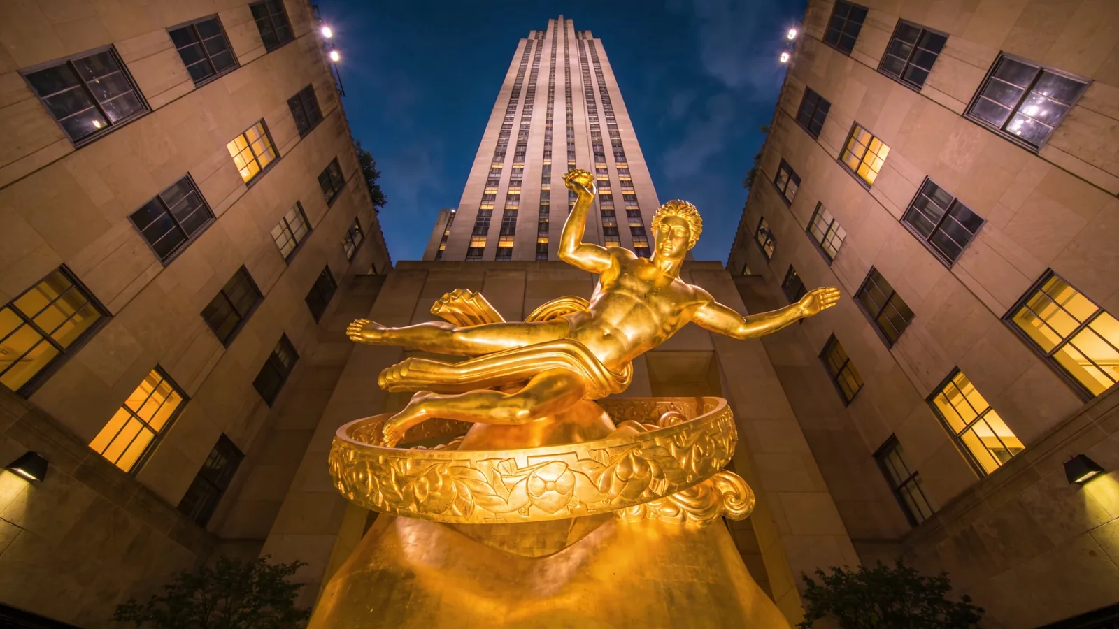 Rockefeller Center plaza at night with Prometheus statue lit and 30 Rockefeller Plaza tower — The Edge vs Top of the Rock midtown side