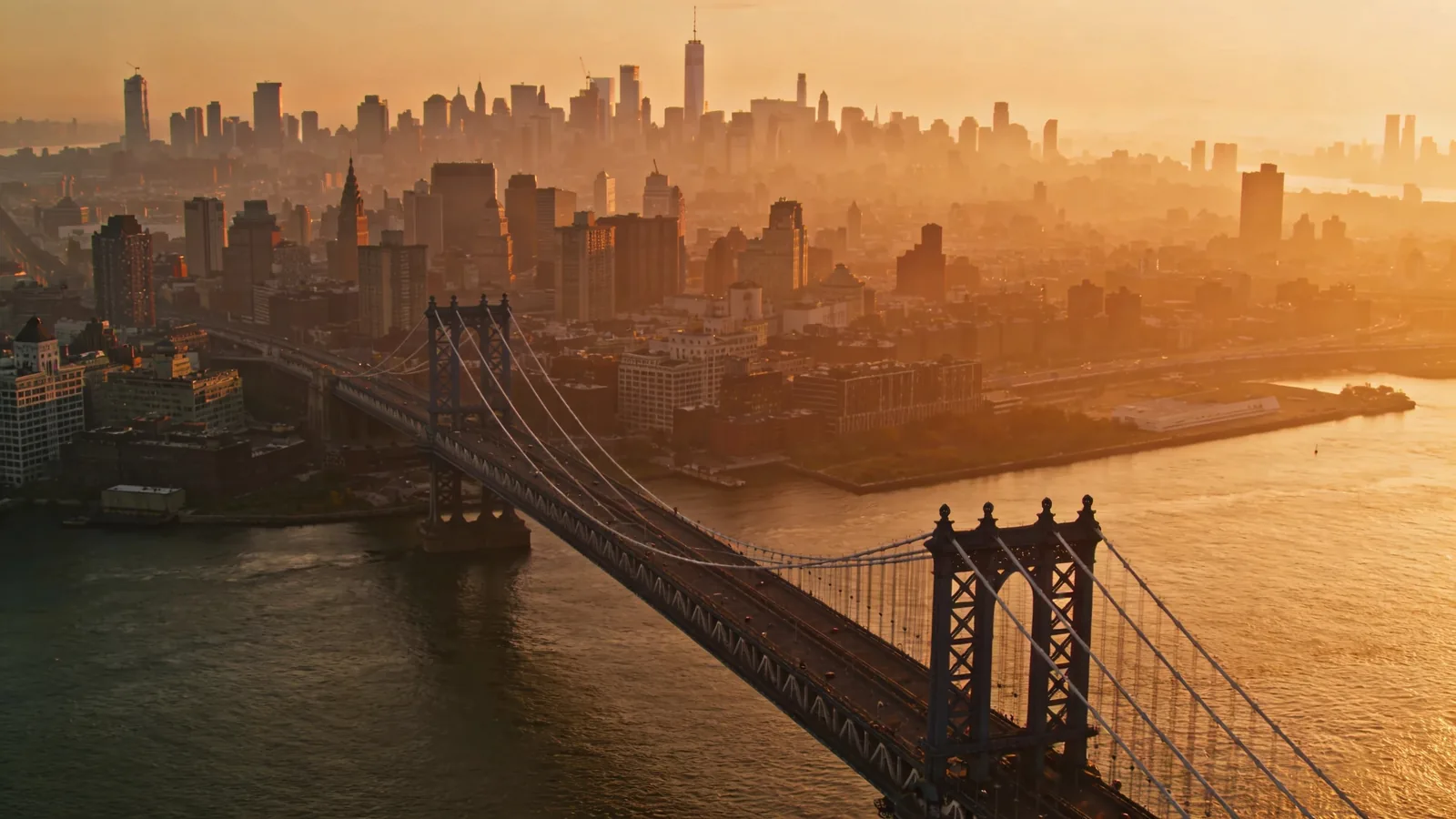 Brooklyn Bridge from a high downtown vantage point with Brooklyn skyline beyond at golden hour — Top of the Rock vs One World Observatory east view