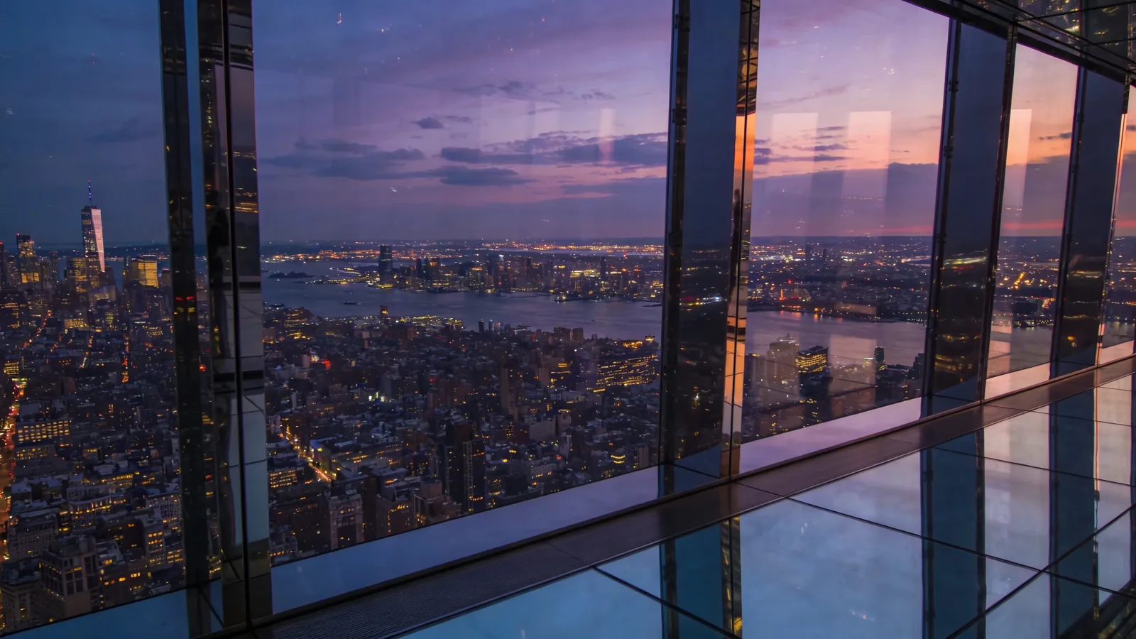 View from a high enclosed glass observation deck at deep twilight with city lights — Empire State sunset tickets 102nd floor transition