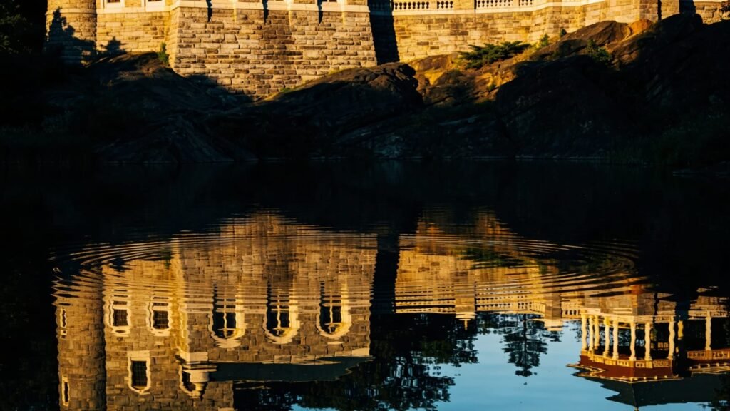Autumn light over a Central Park lake with a historic stone structure reflected in the water.